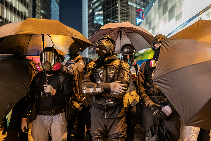 people with masks standing holding umbrellas