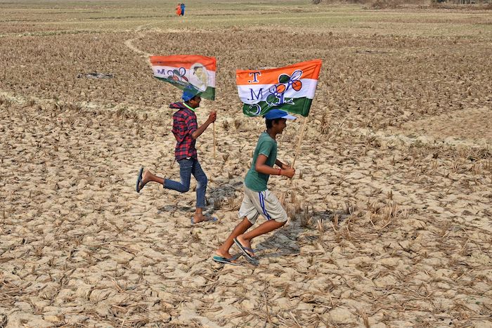 Boys in India run across rice paddy field with political flags