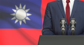 speaker at podium with Taiwan flag in background