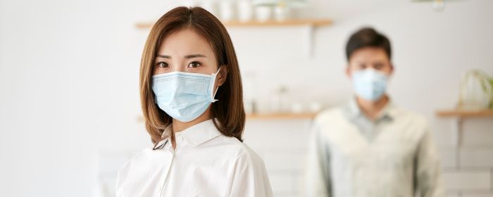 portrait of a young asian woman wearing mask looking at camera with wife in the background